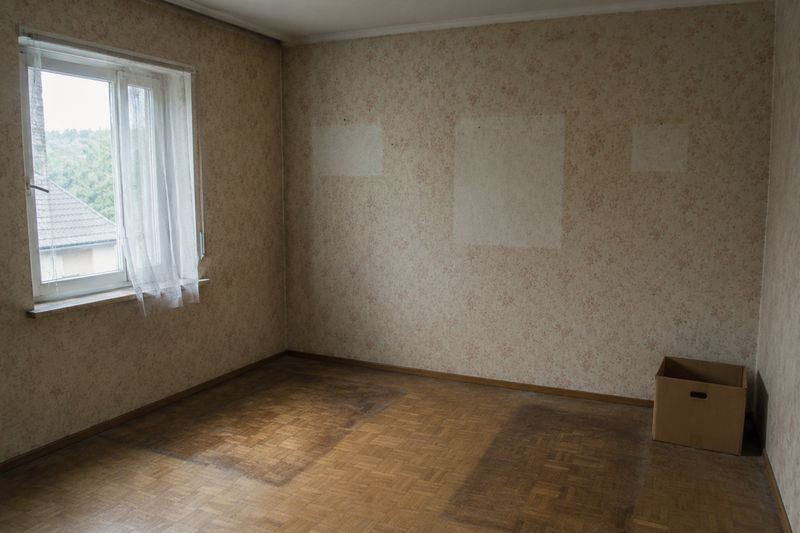 Leergeräumtes Zimmer mit Blümchentapete, hellen Flecken an der Wand und dunkleren Stellen im Parkett